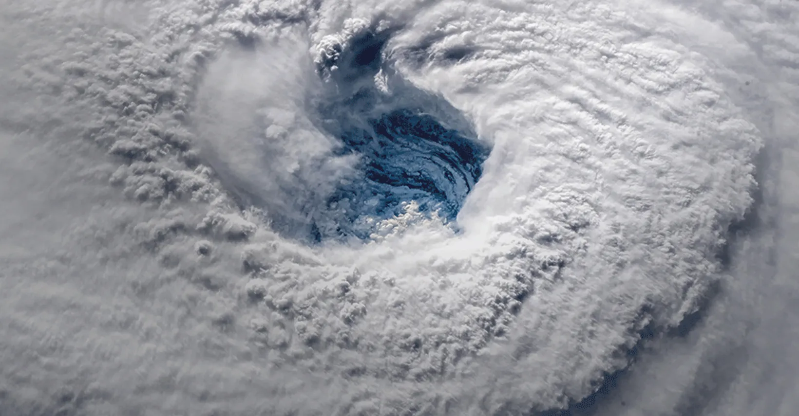 Aerial view of a large spiral storm system with dense white clouds and a central blue eye.