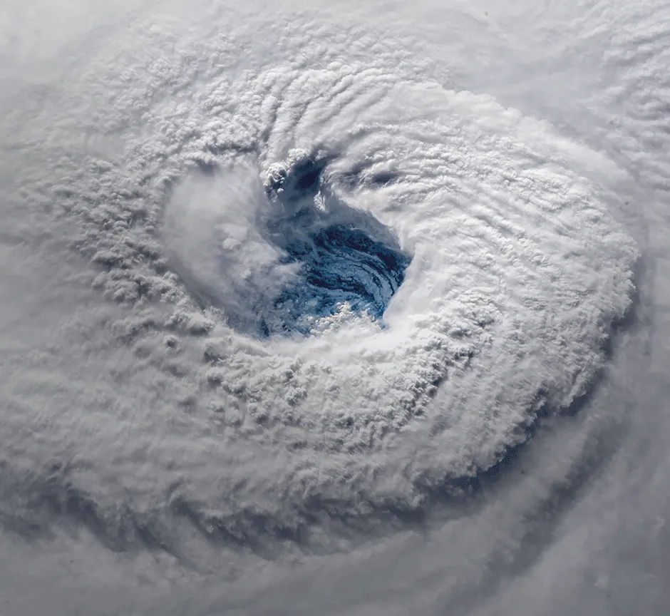 Aerial view of a large spiral storm system with dense white clouds and a central blue eye.