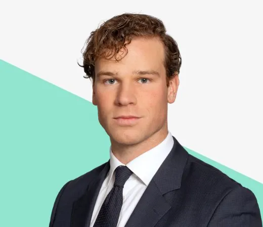 Young man with curly hair in a dark suit and tie against a light background with a teal shape.
