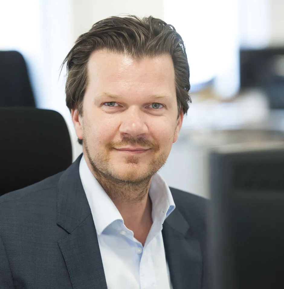 Smiling man in a suit against a geometric background.