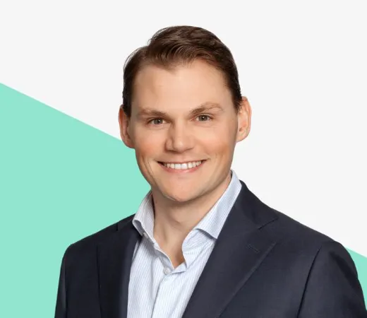 Smiling man in a light blue shirt against a minimalistic background with a teal diagonal shape.