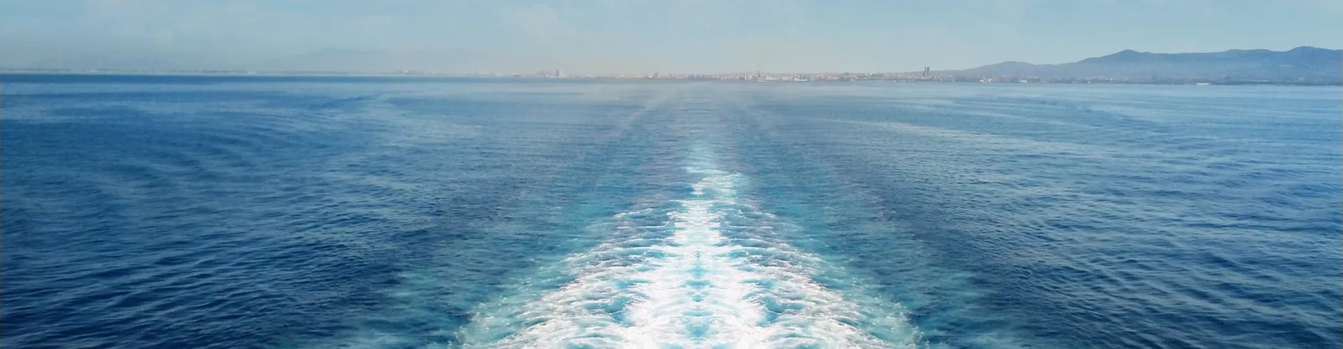 Blue ocean with white wake and scattered clouds.
