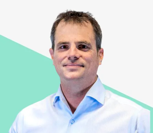 Smiling man with dark hair in a light blue shirt against a light background with a green shape.