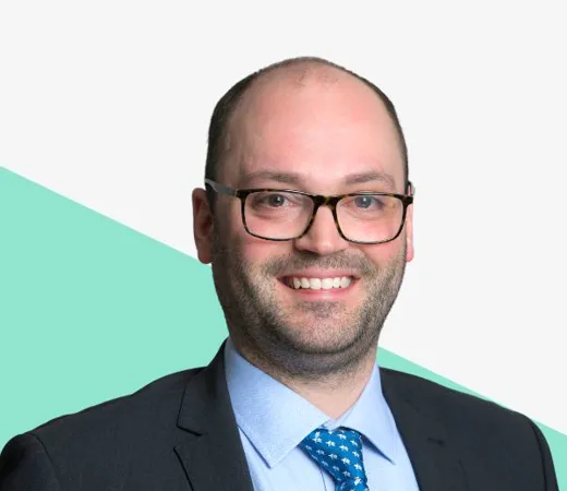Smiling man with glasses in a dark suit against a light background with a geometric green shape.