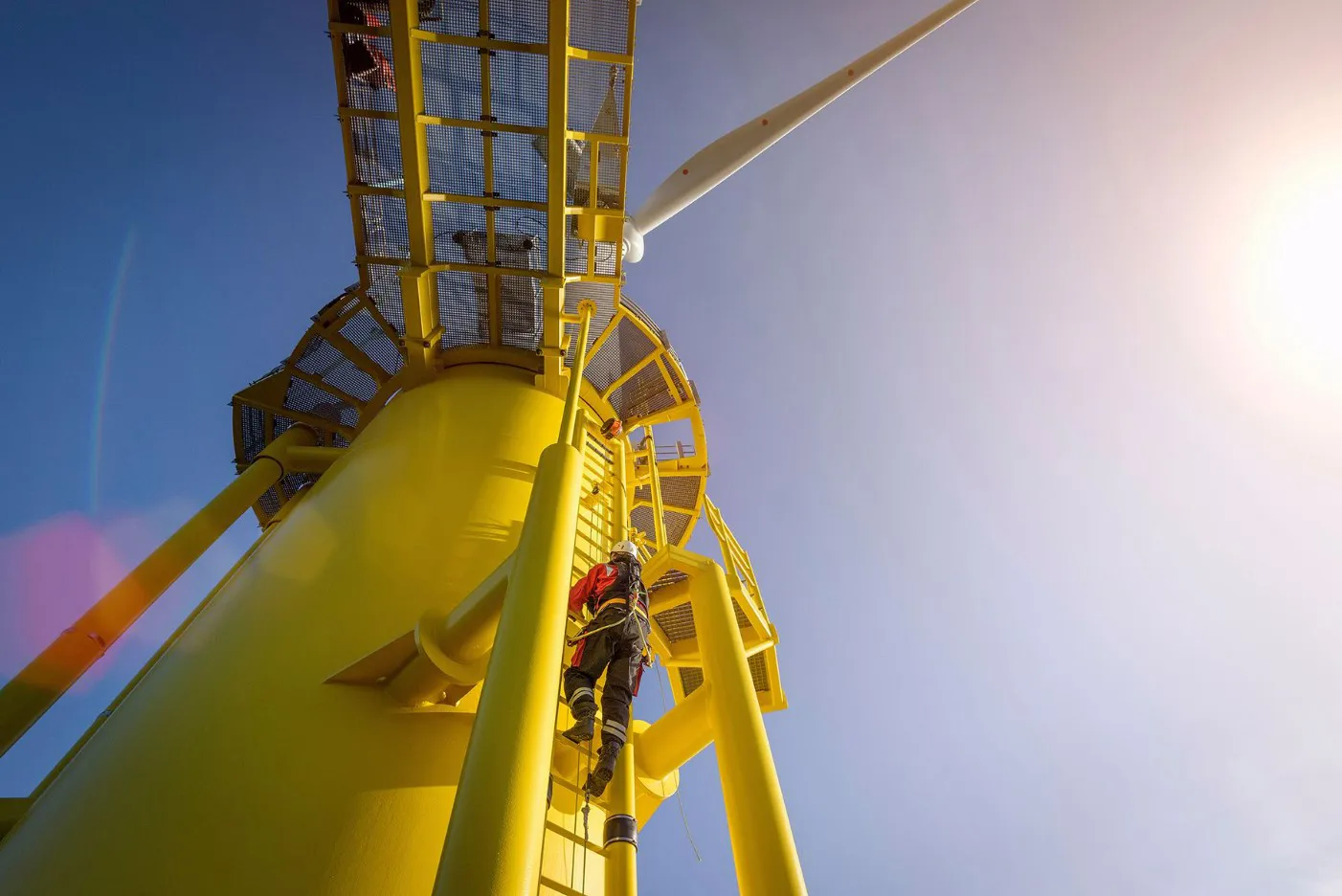 Person in safety gear climbing a bright yellow offshore wind turbine platform.