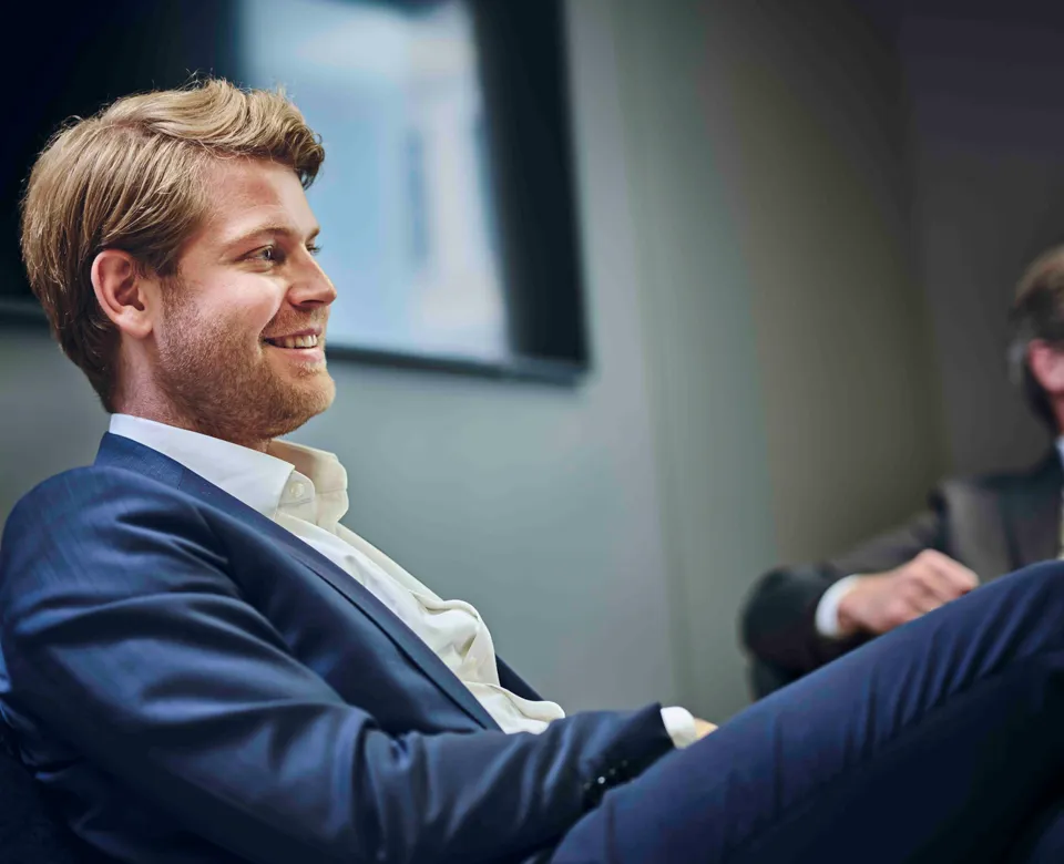 Young man in a dark blue suit sitting in profile, smiling.