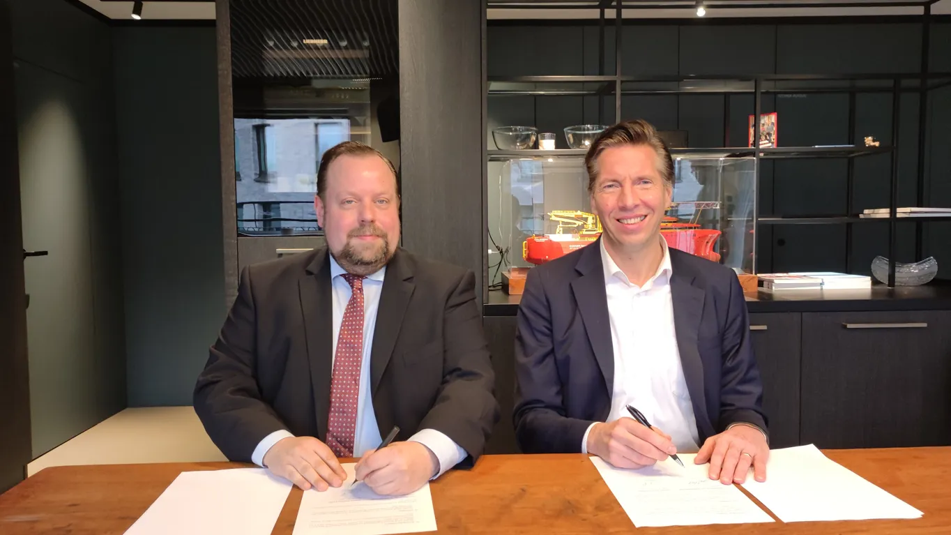 two men sitting at a table signing documents