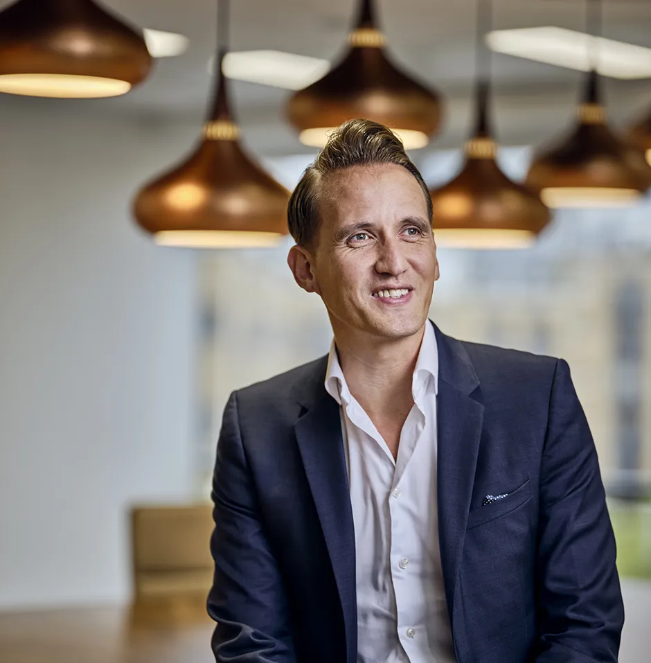 Man in a suit sitting under pendant lights.