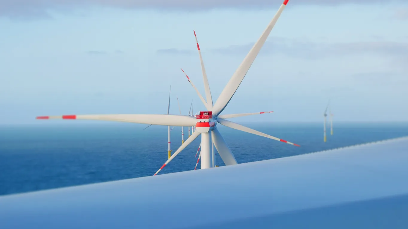 Close-up of a wind turbine with red/white tips against a blue sky and ocean.