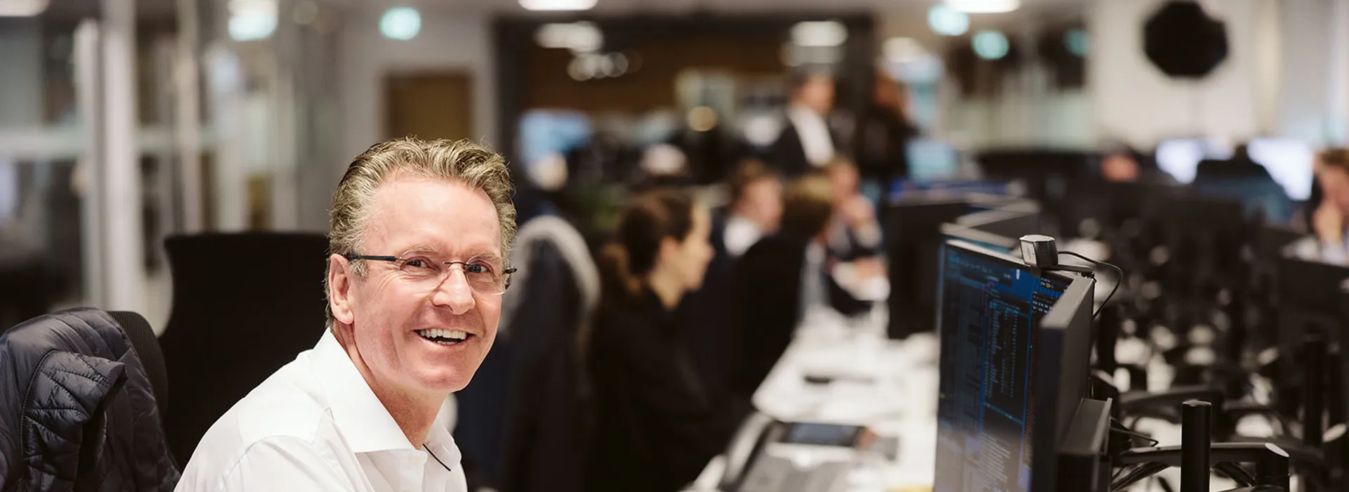 Smiling man at a desk with computer screens.