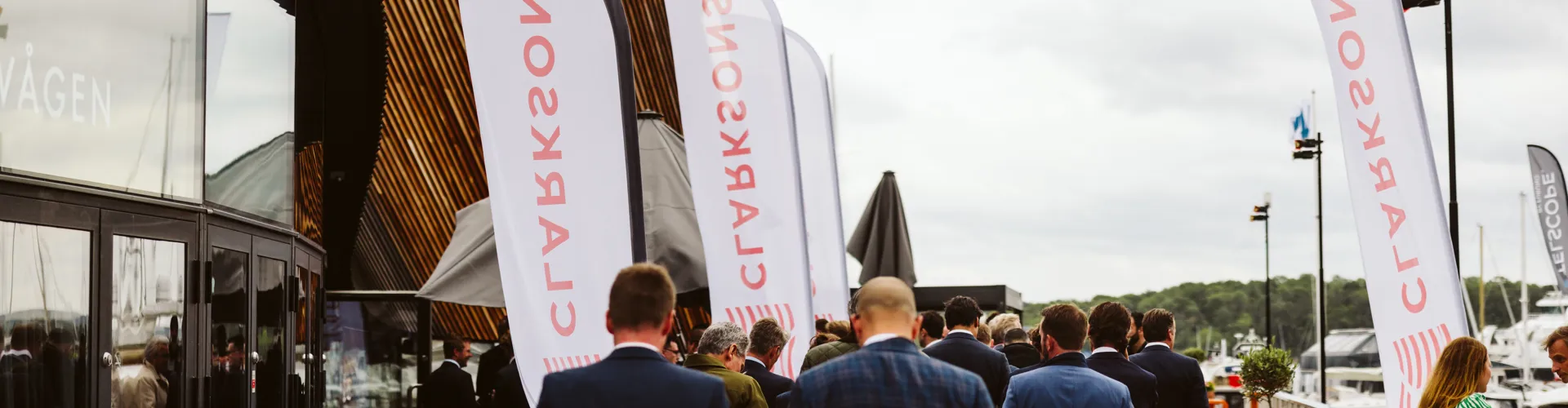 Group in formal attire walking on a deck beside a marina with DEOLS flags.