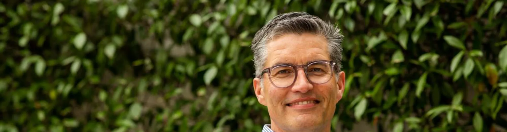 Man smiling with arms crossed, green background.