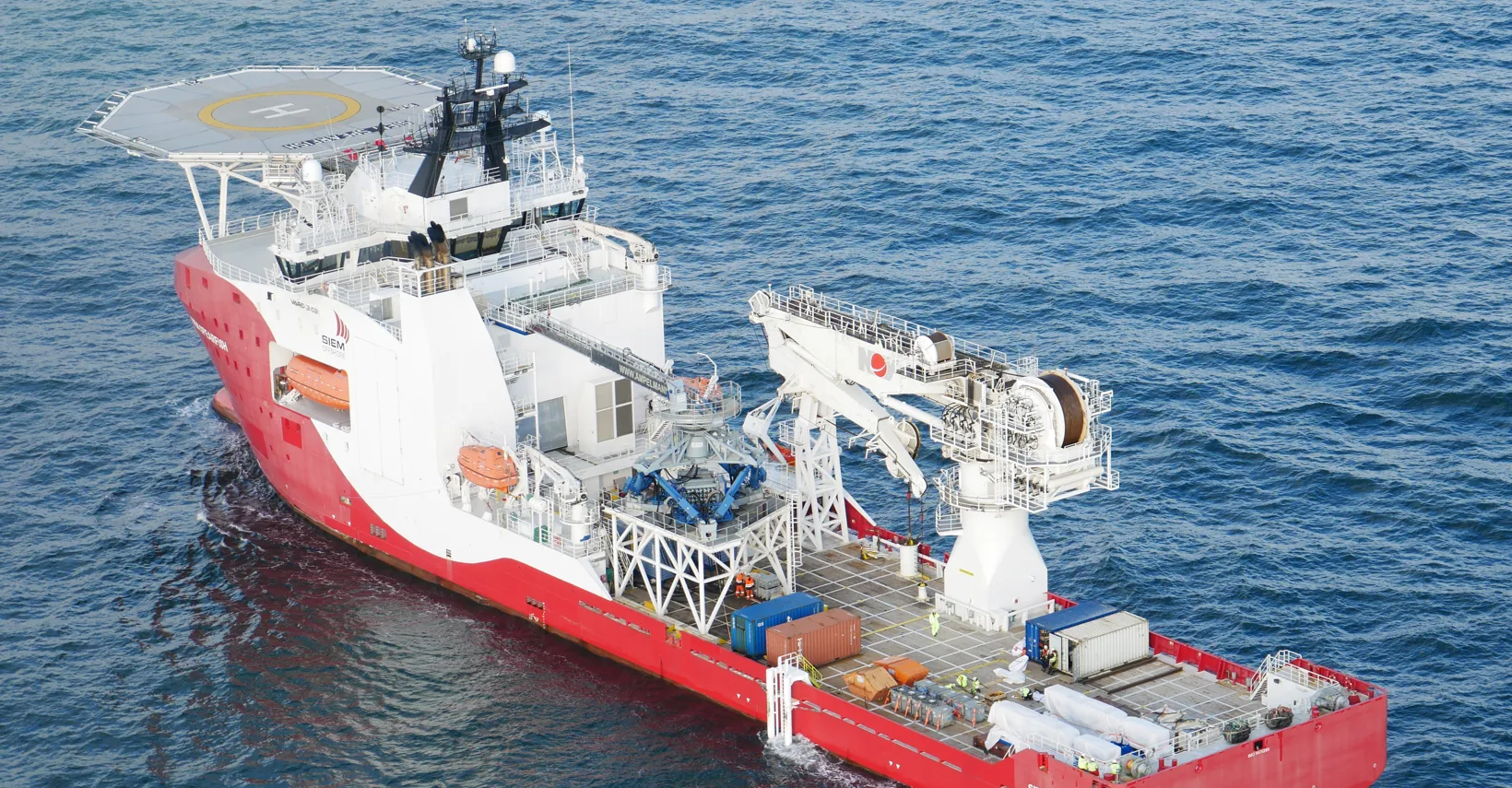 Large multi-deck vessel with a red and white hull on the water, featuring a helipad and crane.