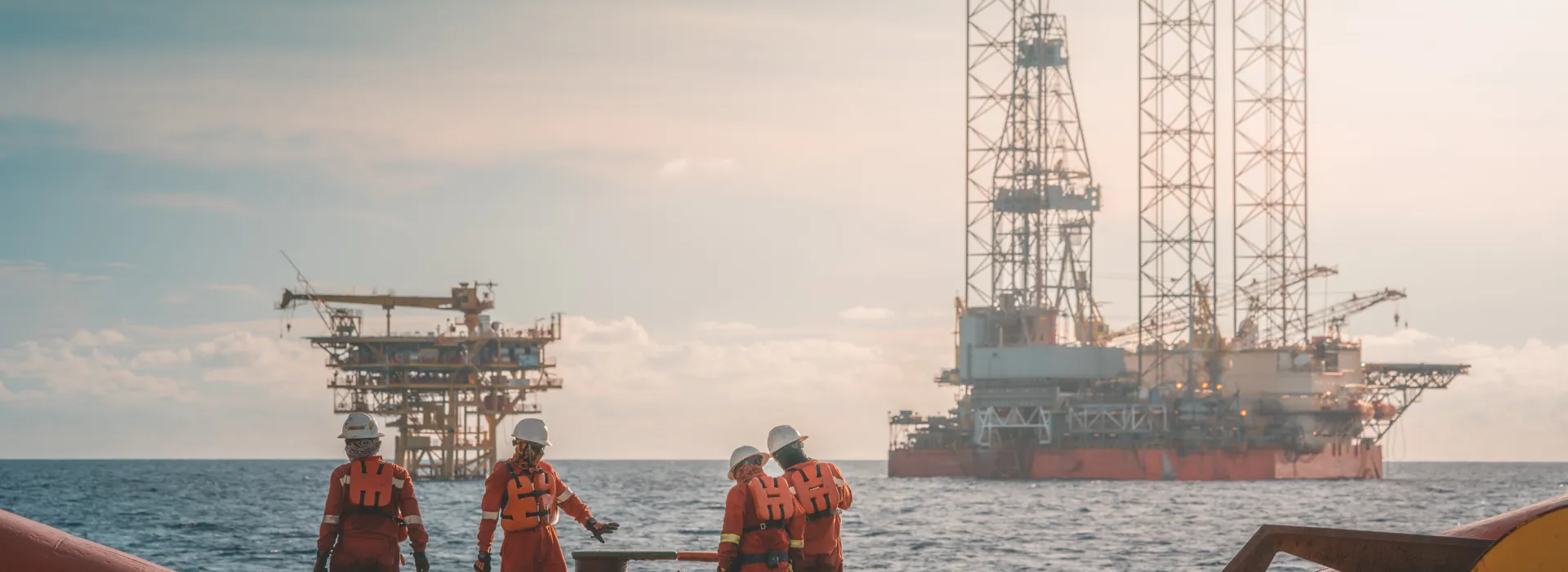 Workers on a platform with oil rigs in background.