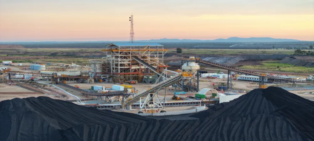 Coal processing facility with coal piles, conveyor belts, and machinery at sunrise.