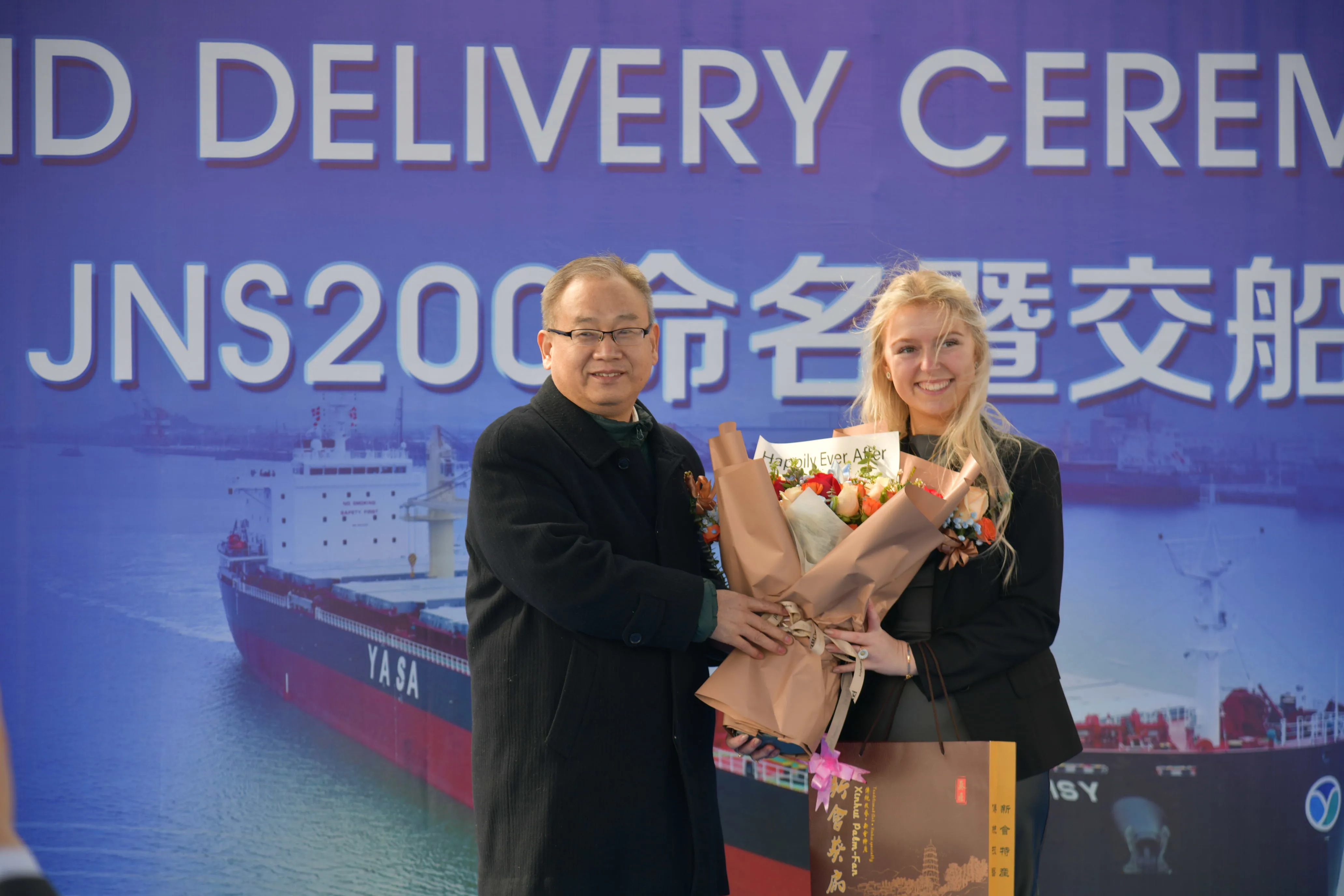 Two people holding flowers at a ceremony backdrop.
