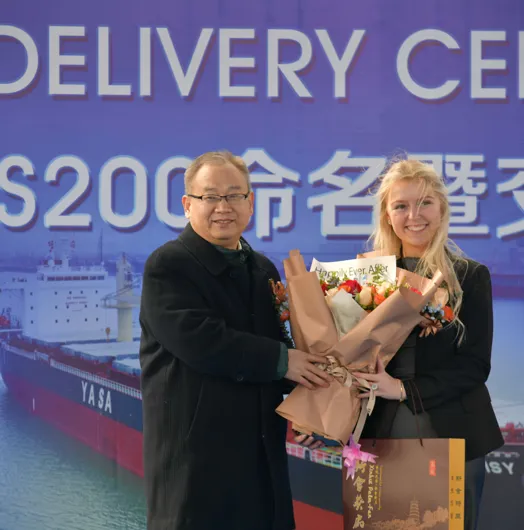 Two people holding flowers at a ceremony backdrop.