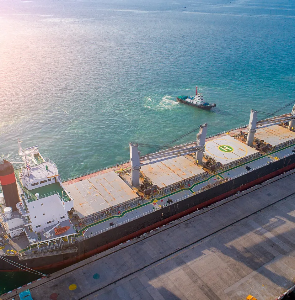Cargo ship at dock with tugboats nearby.