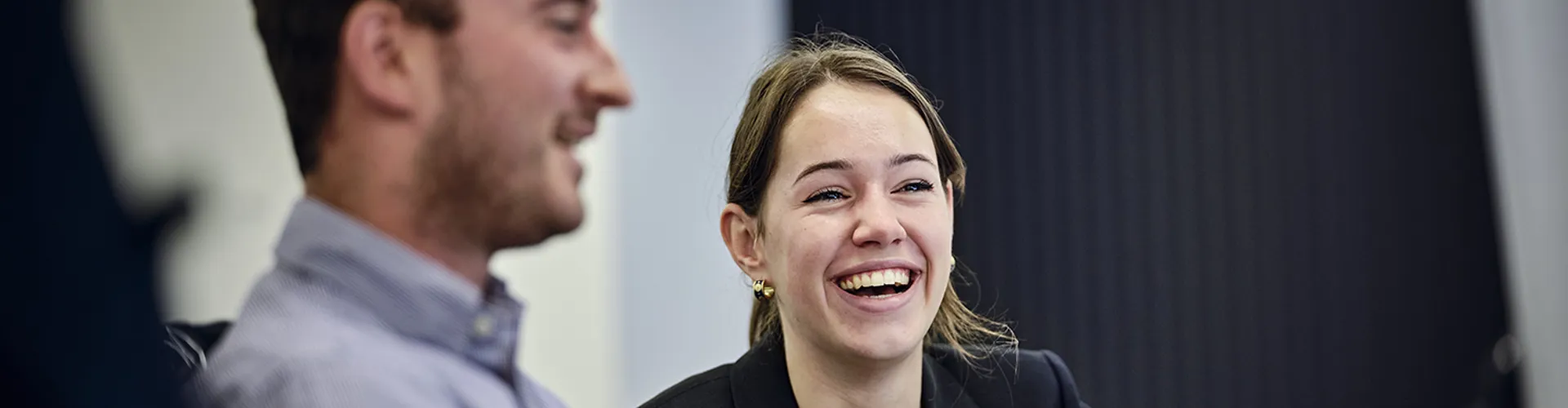 focus on woman smiling at desk whilst discussing with a colleague