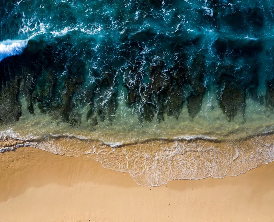 Aerial view of ocean waves meeting sandy beach.