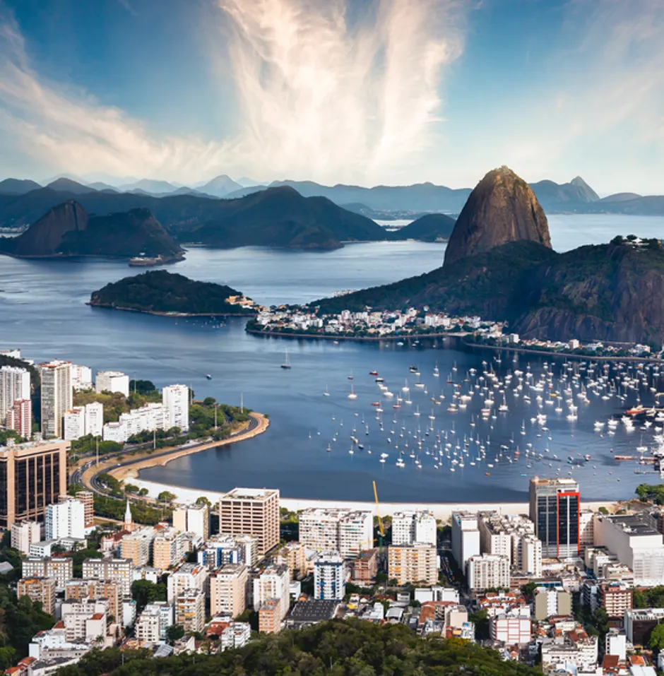 Panoramic view of a coastal city with a waterfront, mixed architecture, and boats on calm water.