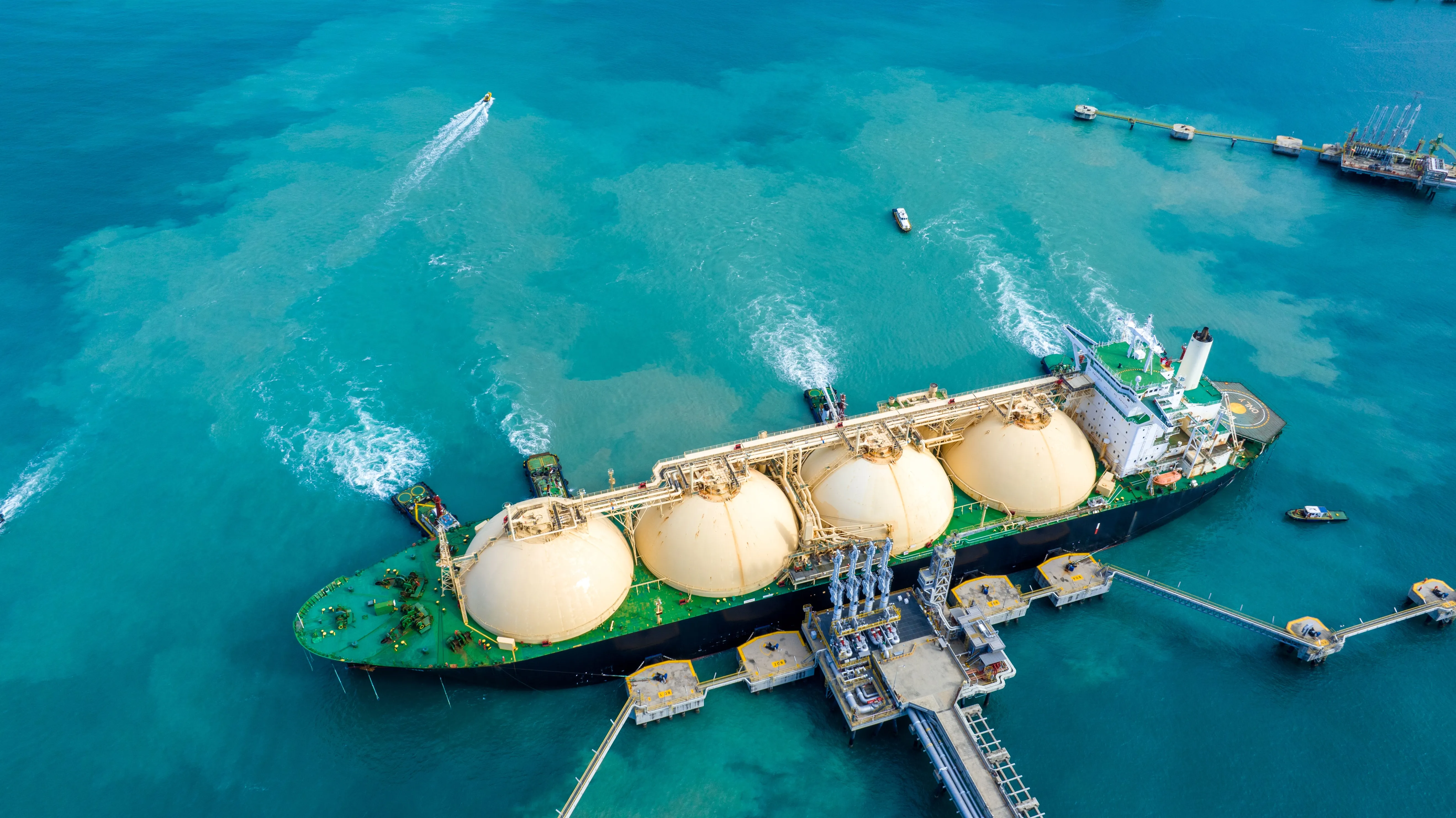 Aerial view of large LNG tanker with spherical tanks anchored near port.