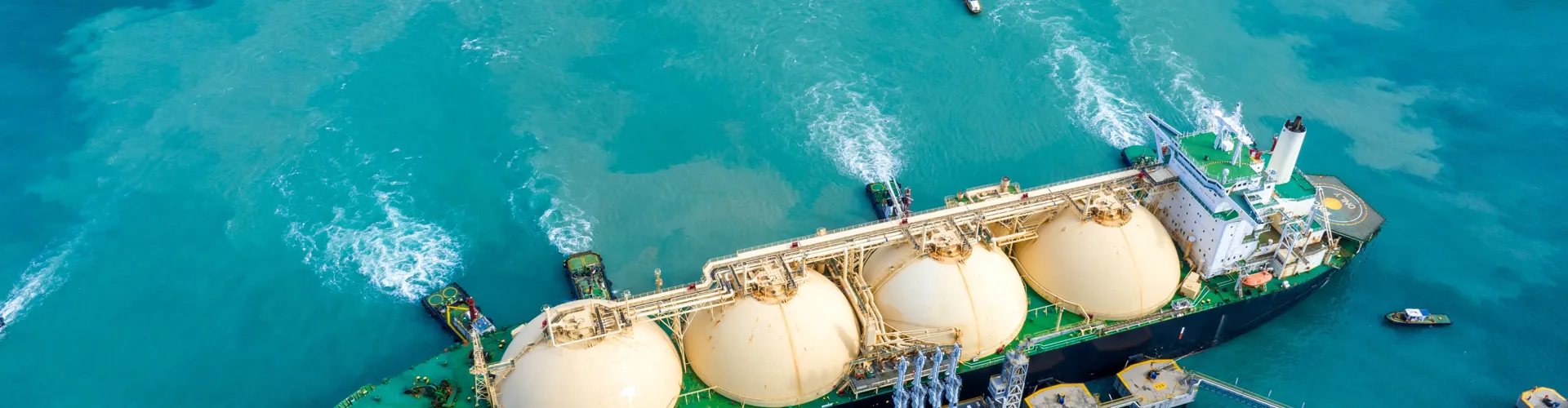 Aerial view of large LNG tanker with spherical tanks anchored near port.