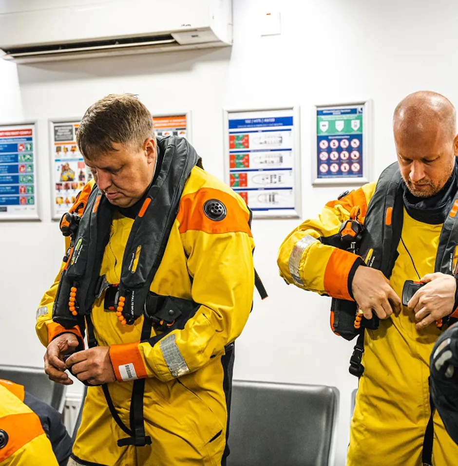 Two individuals in yellow safety suits adjust gear.