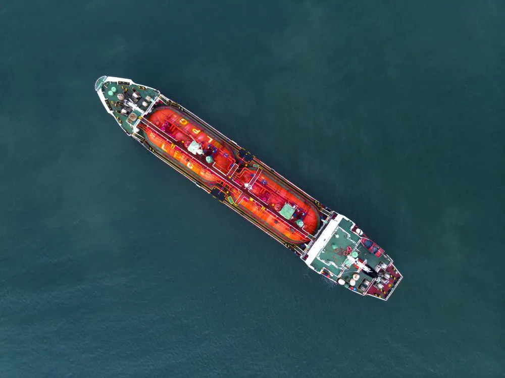 Aerial view of a large red and green cargo ship floating on calm blue water.