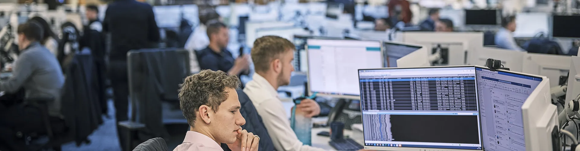 Office workers at computers in a busy workspace.