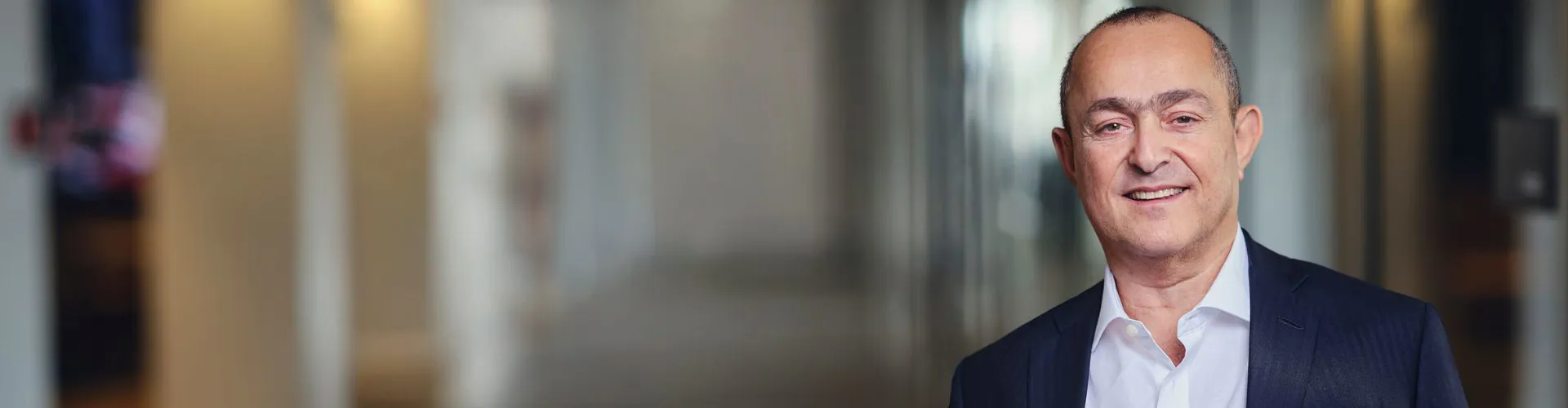 Smiling man in a suit, blurred indoor background.