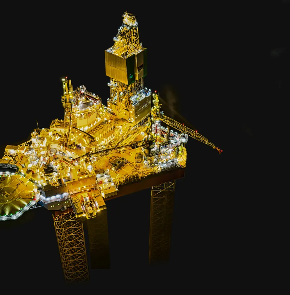 Illuminated oil rig against a dark background.