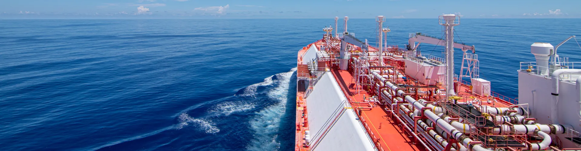 Large cargo ship sailing on calm blue water under a clear sky, leaving a gentle wake.