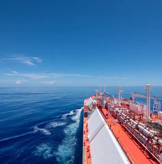 Large cargo ship sailing on calm blue water under a clear sky, leaving a gentle wake.