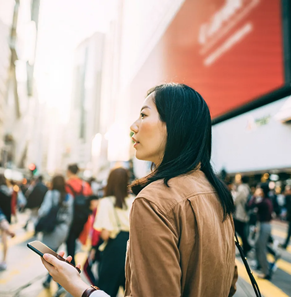 Young woman checking on mobile phone while crossing street and commuting in busy downtown city street