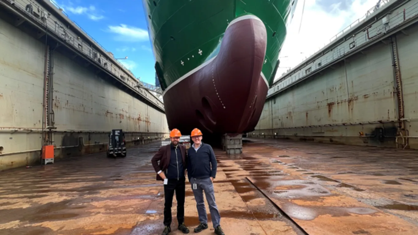 two men standing in front of a dry docked boat