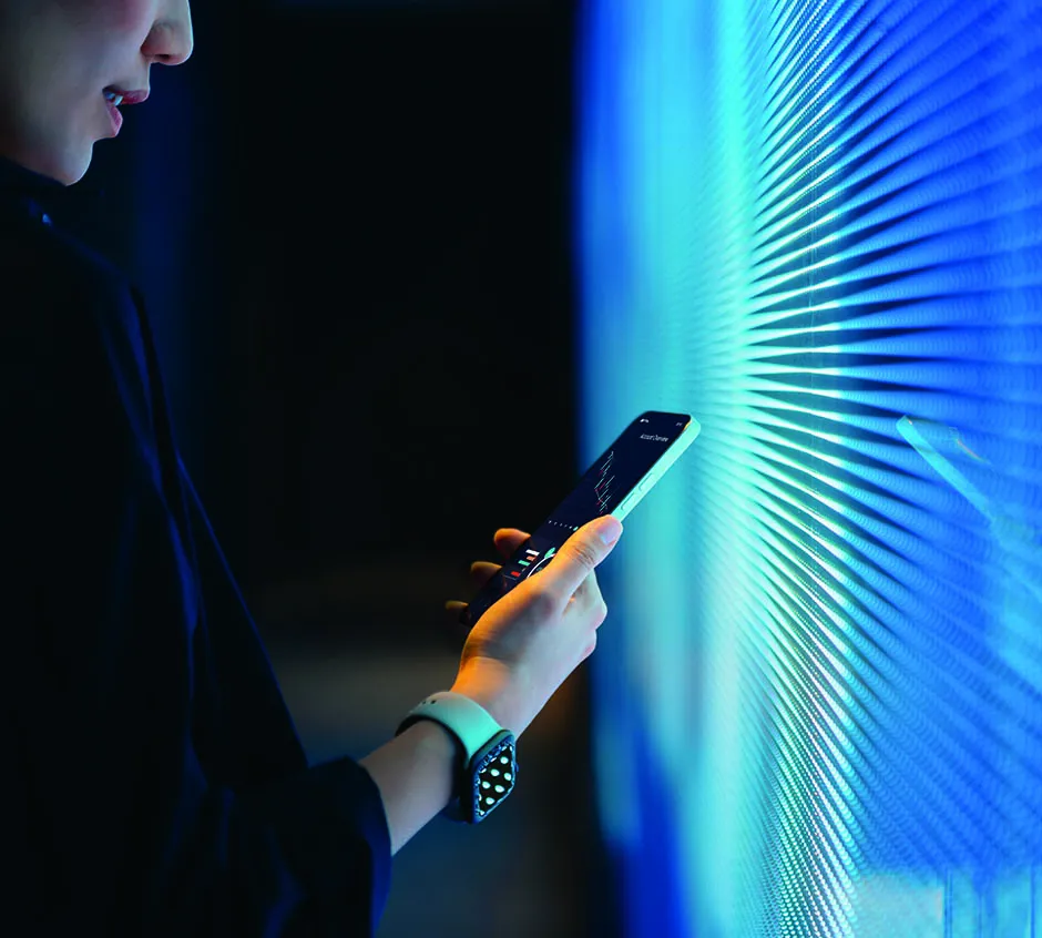 Hand holding a smartphone in front of a vibrant blue illuminated wall.