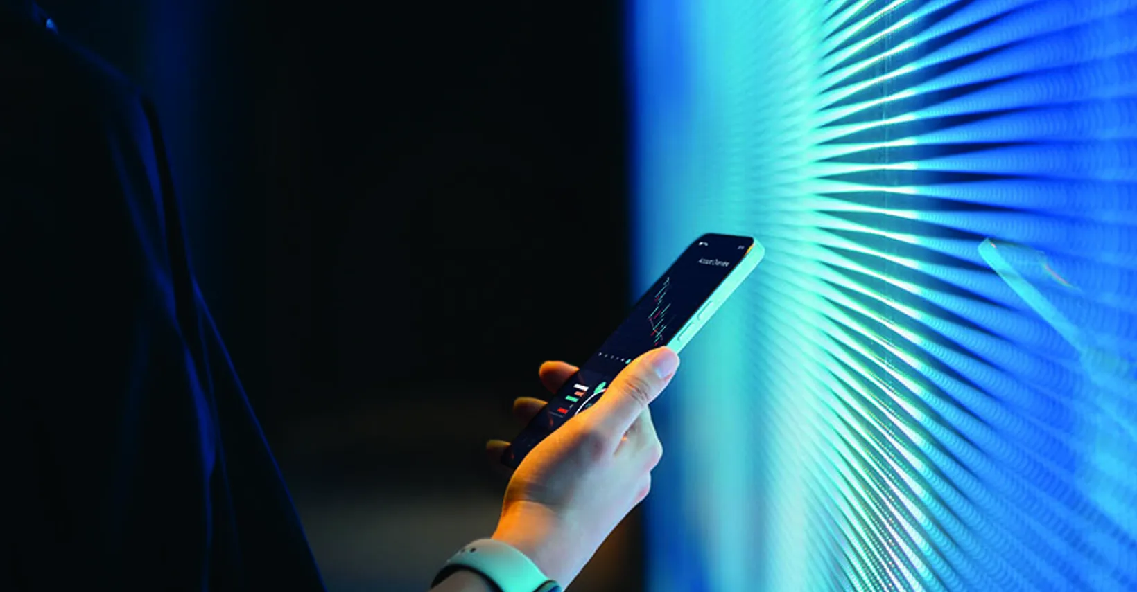 Hand holding a smartphone in front of a vibrant blue illuminated wall.