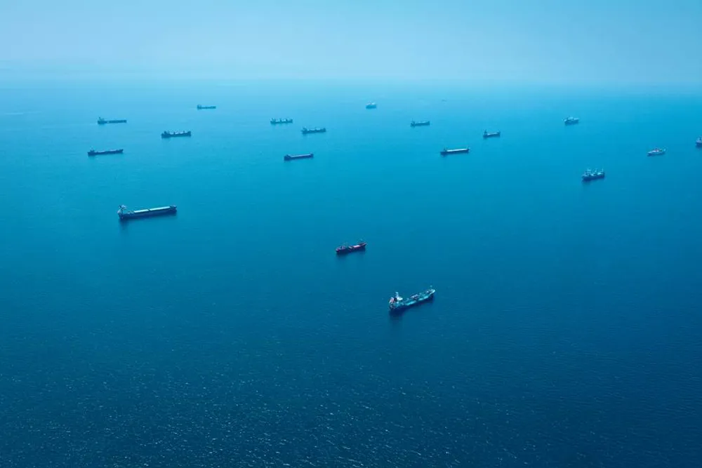 Aerial view of numerous cargo ships scattered across a calm, clear blue ocean.