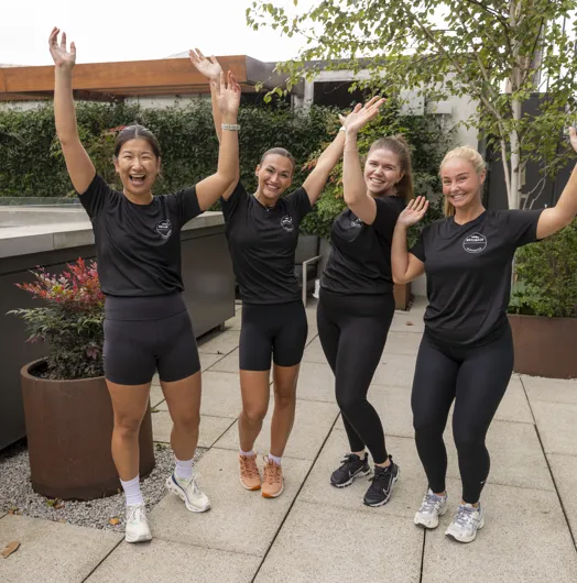 Four women in black athletic shirts posing with raised arms on a patio.