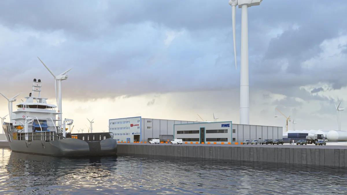Large ship docked at a port near industrial buildings and wind turbines.
