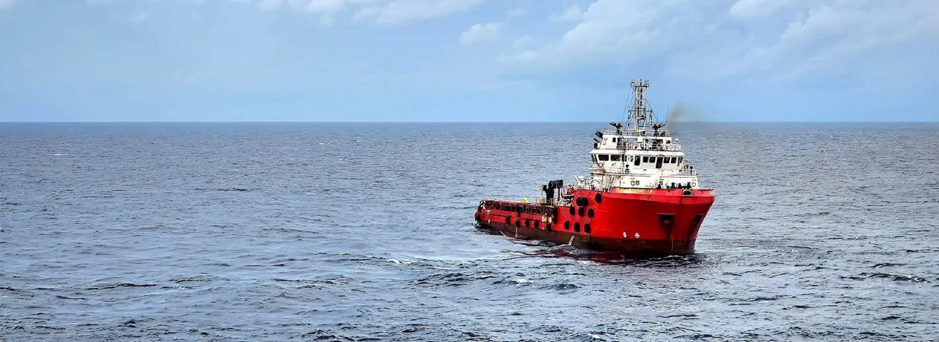 Red ship navigating calm ocean waters under a partly cloudy sky.