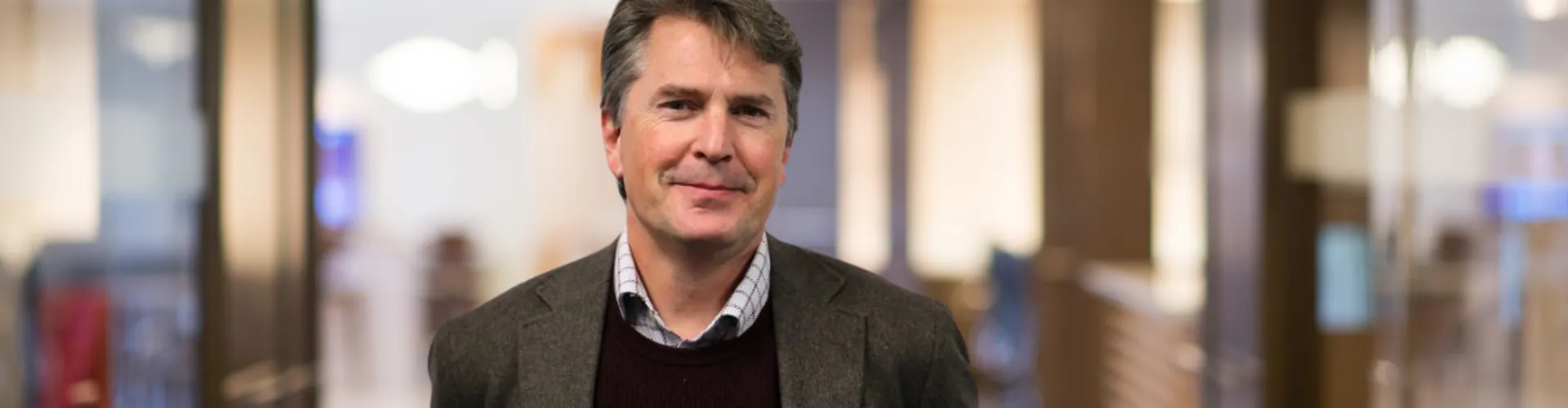 Man in a blazer smiling inside an office.